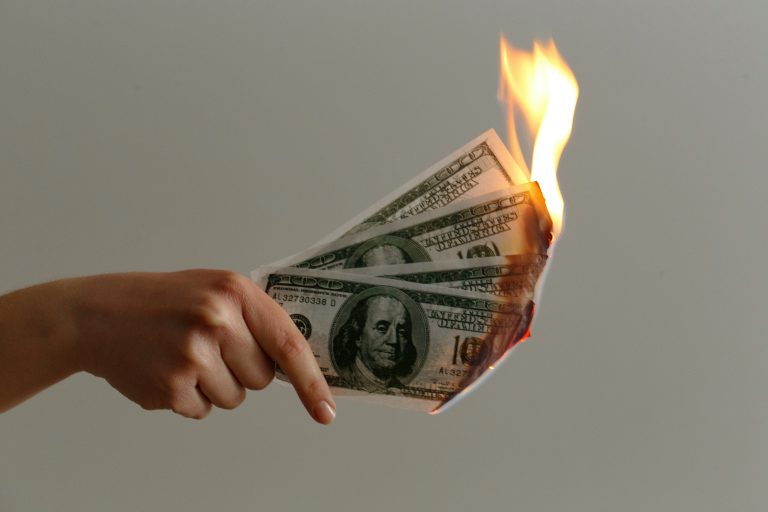Main tenant des billets en feu, illustration symbolique d’un article sur le gaspillage d'argent dans les agences de conception de sites web peu fiables